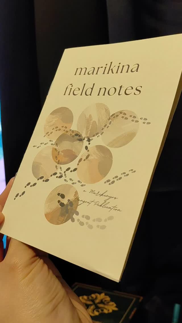 A hand holding a Marikina Field Notes notebook, its cream cover printed with painted circles and trails of footprints
